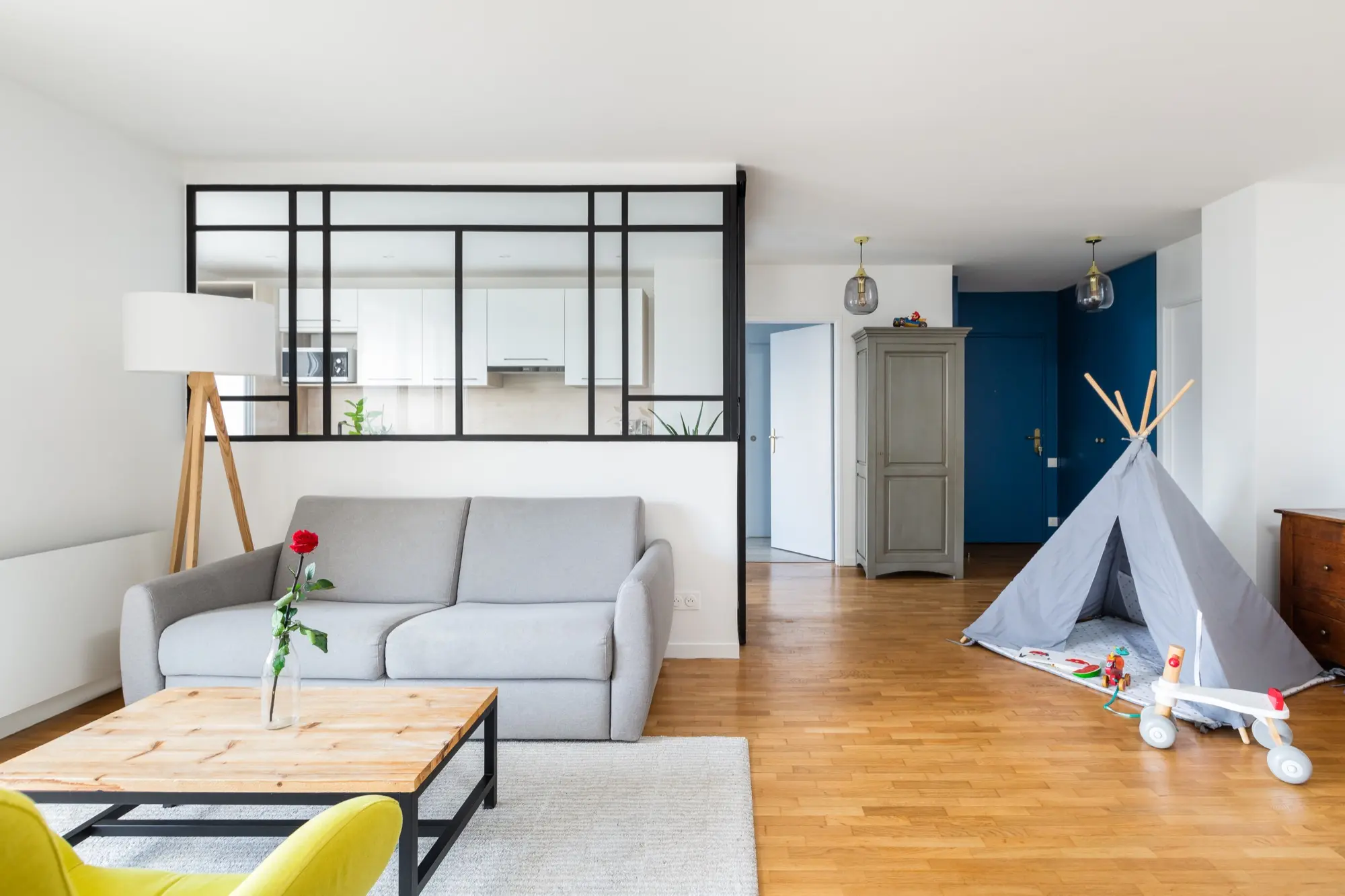 Salon avec canapé gris, parquet et verrière donnant sur une cuisine blanche — réalisation Luc par O2R